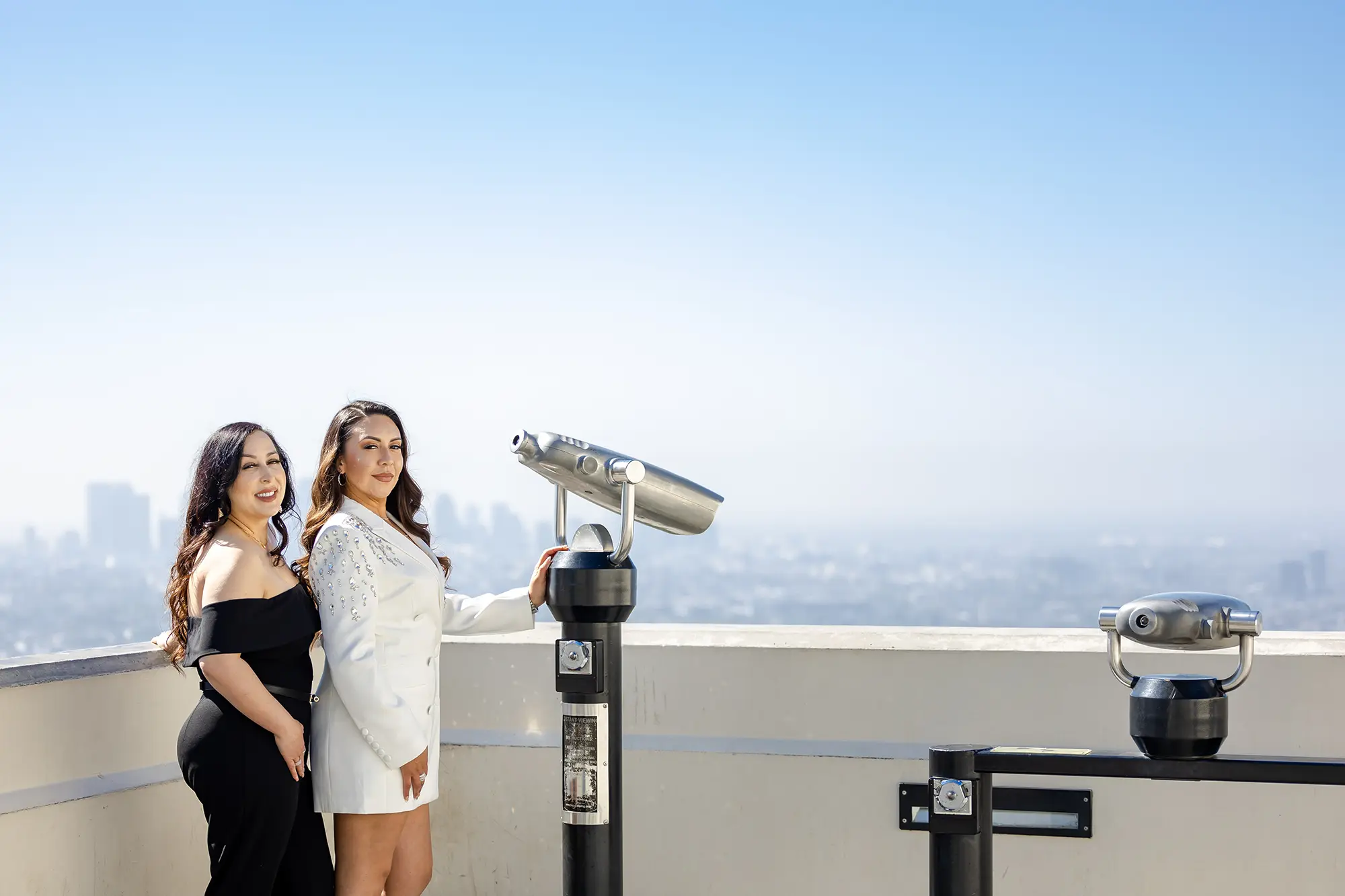 Engagement photo of female LGBT couple standing next to the binoculars with city scape at Griffith Park Observatory, NZ WEDDING STUDIO